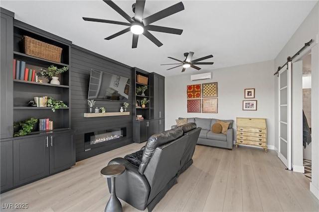 living room featuring ceiling fan, a barn door, built in features, a fireplace, and light wood-type flooring