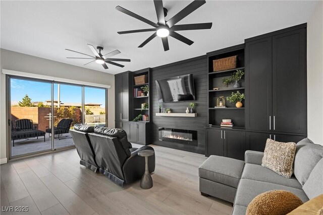 living room with a fireplace, built in shelves, light wood-type flooring, and ceiling fan