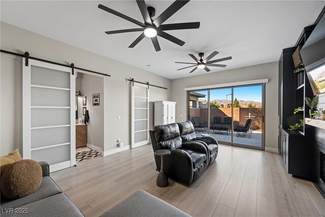 living room featuring ceiling fan, a barn door, and light hardwood / wood-style floors