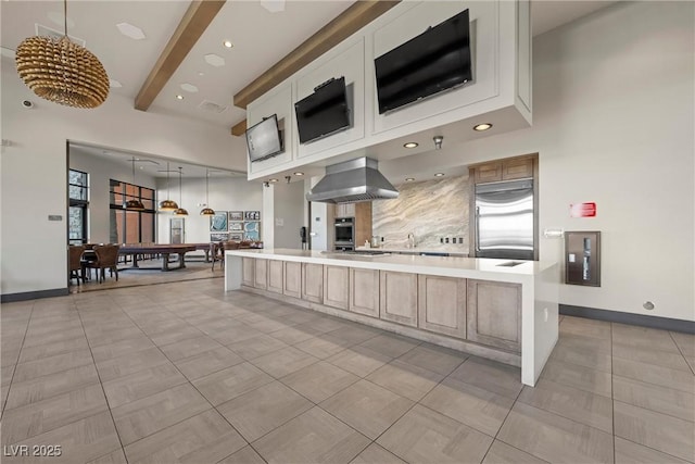 kitchen with pendant lighting, white cabinets, wall chimney range hood, appliances with stainless steel finishes, and beamed ceiling