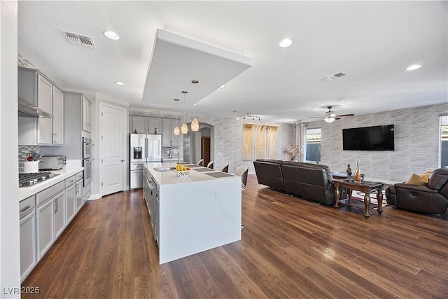 kitchen with gray cabinetry, hanging light fixtures, dark hardwood / wood-style floors, a center island with sink, and appliances with stainless steel finishes