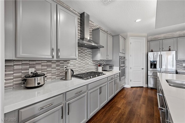 kitchen with decorative backsplash, appliances with stainless steel finishes, dark wood-type flooring, wall chimney range hood, and gray cabinets