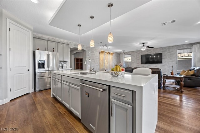 kitchen featuring gray cabinetry, ceiling fan, sink, stainless steel appliances, and a center island with sink