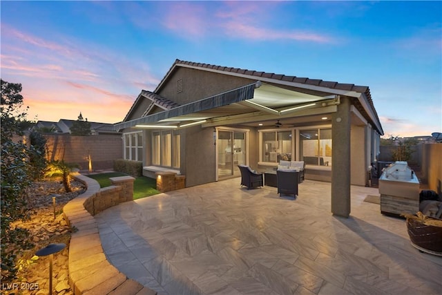 back house at dusk with outdoor lounge area, an outdoor kitchen, and a patio area