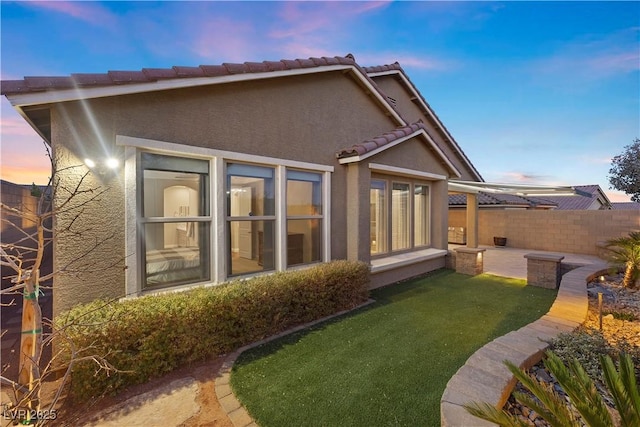 back house at dusk featuring a yard and a patio