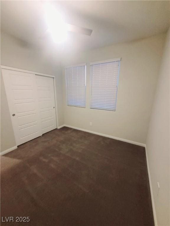 unfurnished bedroom featuring dark colored carpet, a closet, and ceiling fan