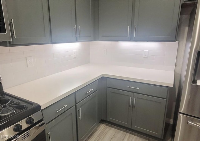 kitchen featuring decorative backsplash, gray cabinets, light wood-type flooring, and stainless steel appliances