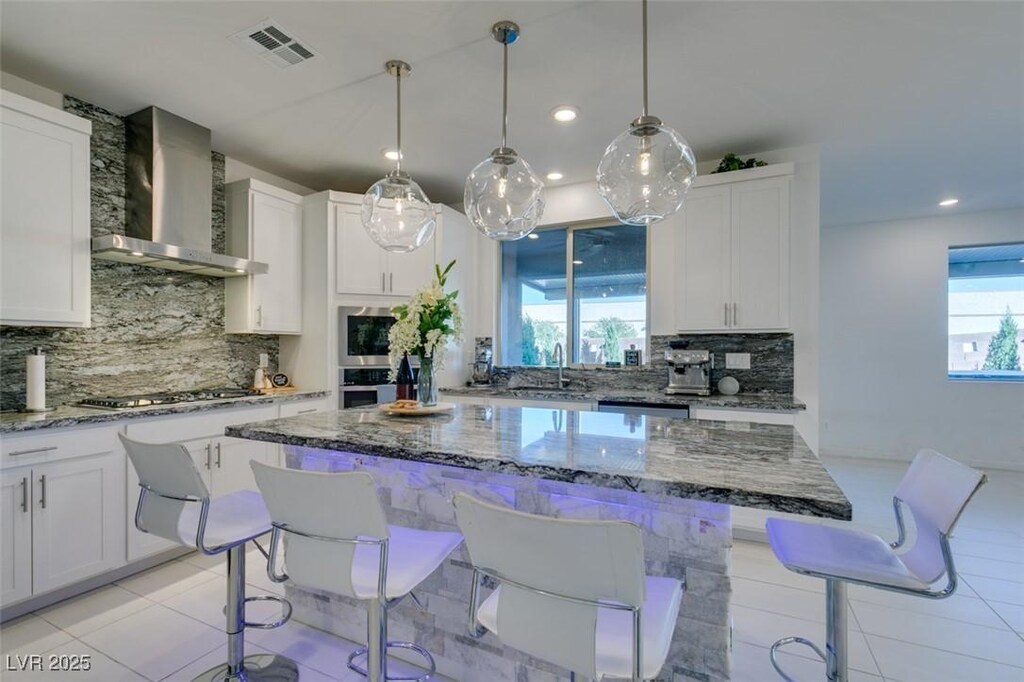 kitchen with white cabinetry, a center island, wall chimney range hood, tasteful backsplash, and appliances with stainless steel finishes