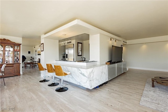 kitchen featuring a kitchen breakfast bar, light hardwood / wood-style floors, stainless steel built in refrigerator, and kitchen peninsula