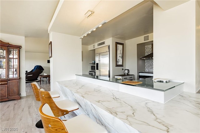 kitchen with kitchen peninsula, light hardwood / wood-style flooring, built in fridge, and range hood