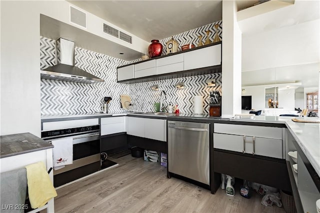 kitchen featuring white cabinetry, sink, wall chimney range hood, light hardwood / wood-style flooring, and appliances with stainless steel finishes