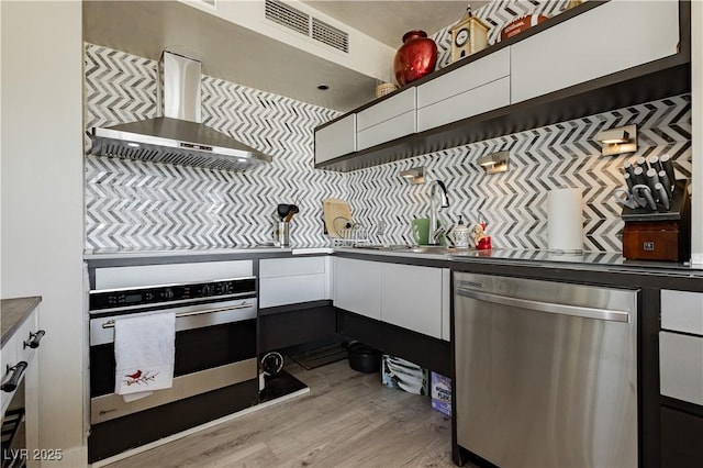 kitchen featuring appliances with stainless steel finishes, light hardwood / wood-style flooring, white cabinetry, and wall chimney range hood