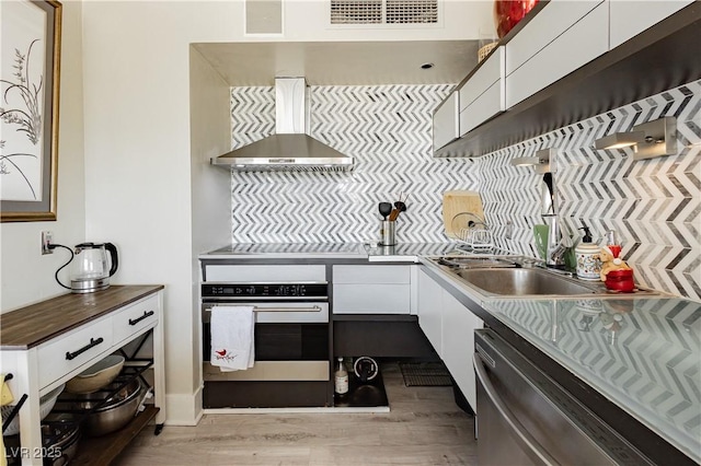 kitchen with dishwasher, white cabinets, oven, wall chimney exhaust hood, and light hardwood / wood-style floors