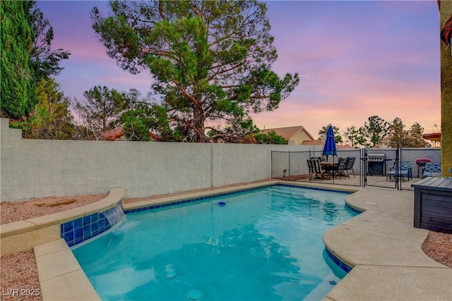 pool at dusk with pool water feature and a patio area