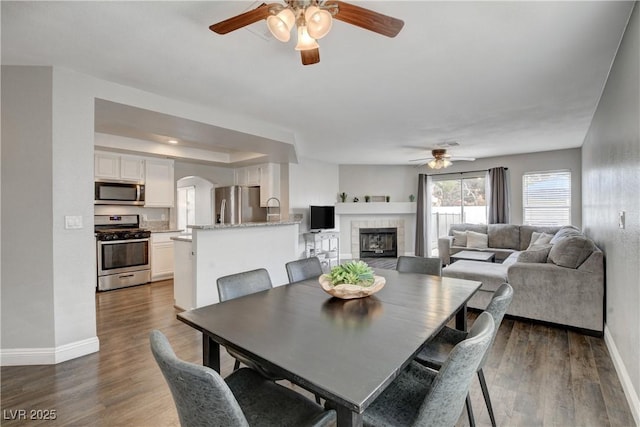 3320 Haven Beach Way, Las Vegas, NV 89117 - dining room with a ceiling fan, baseboards, arched walkways, a fireplace, and wood finished floors