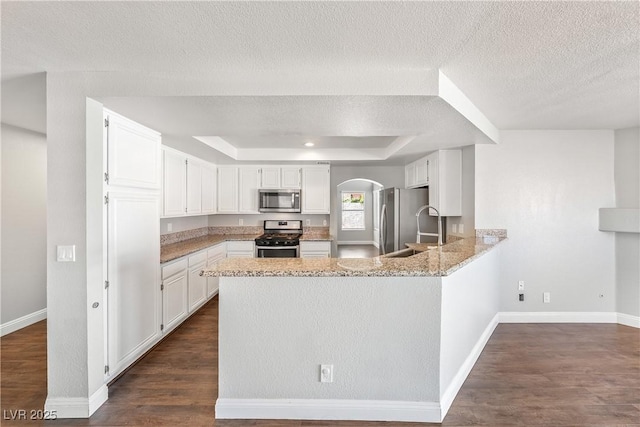 3320 Haven Beach Way, Las Vegas, NV 89117 - kitchen with stainless steel appliances, arched walkways, a peninsula, a tray ceiling, and a textured ceiling