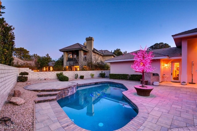 pool at dusk with a fire pit and a patio area