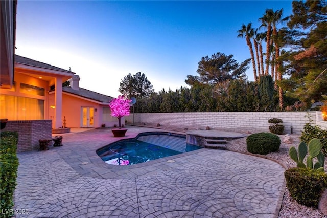 pool at dusk featuring a jacuzzi, french doors, and a patio area