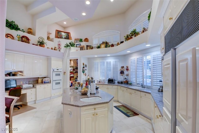 kitchen with high end fridge, white double oven, a towering ceiling, and sink