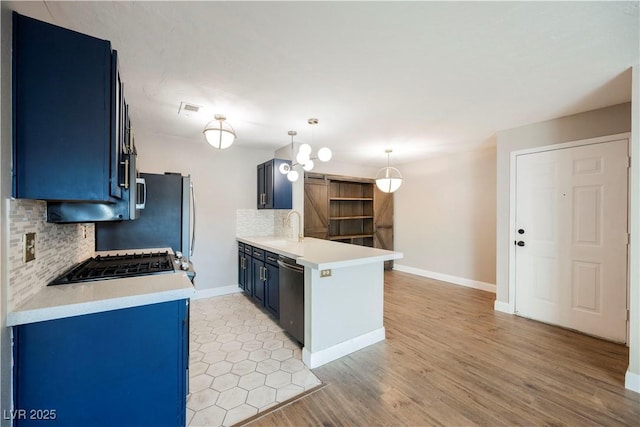 kitchen featuring dishwasher, blue cabinets, hanging light fixtures, decorative backsplash, and kitchen peninsula