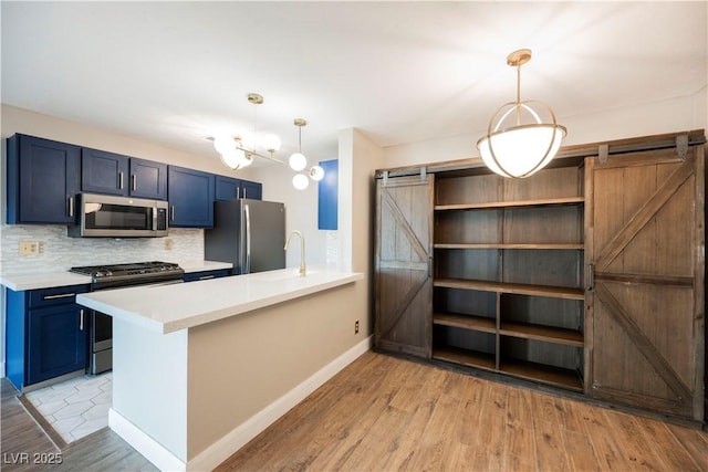 kitchen with a barn door, kitchen peninsula, decorative light fixtures, and appliances with stainless steel finishes