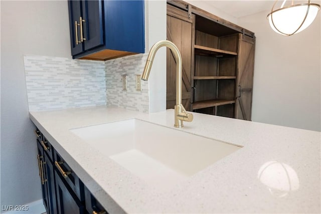 kitchen featuring sink, tasteful backsplash, a barn door, light stone counters, and blue cabinets