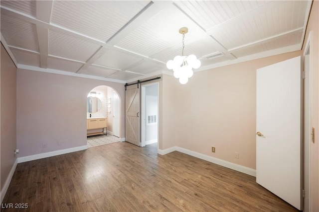 empty room featuring hardwood / wood-style flooring, a barn door, coffered ceiling, and an inviting chandelier