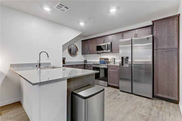 kitchen with sink, light hardwood / wood-style flooring, light stone counters, kitchen peninsula, and stainless steel appliances