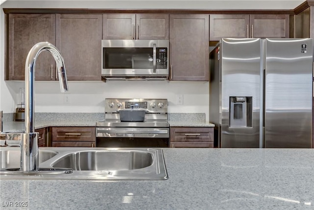 kitchen featuring dark brown cabinetry, light stone counters, and stainless steel appliances