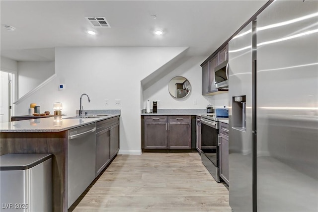 kitchen with sink, dark brown cabinets, light stone counters, kitchen peninsula, and stainless steel appliances