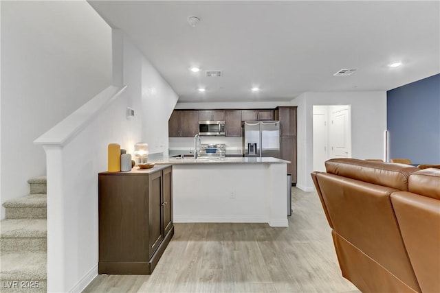 kitchen with sink, dark brown cabinetry, light hardwood / wood-style floors, kitchen peninsula, and stainless steel appliances