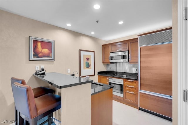 kitchen featuring paneled refrigerator, gas cooktop, kitchen peninsula, oven, and a breakfast bar