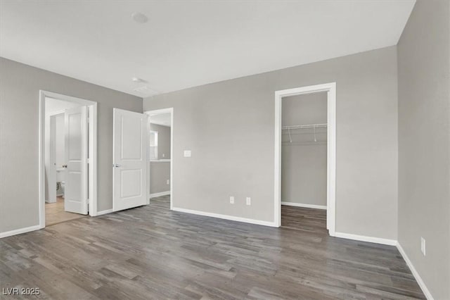 unfurnished bedroom featuring connected bathroom, wood finished floors, baseboards, a closet, and a walk in closet