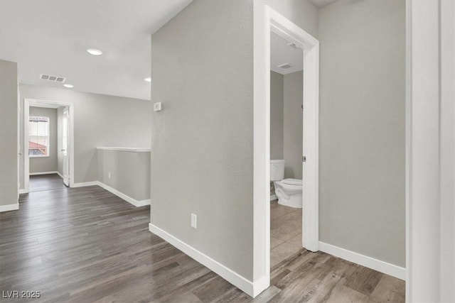 hallway featuring baseboards, visible vents, and wood finished floors