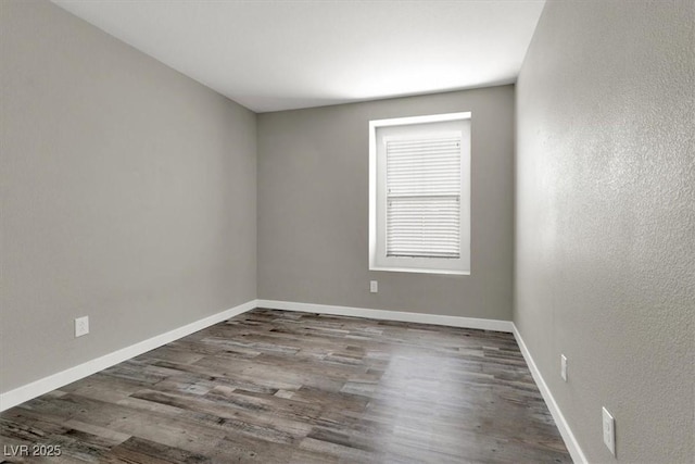 spare room featuring a textured wall, wood finished floors, and baseboards