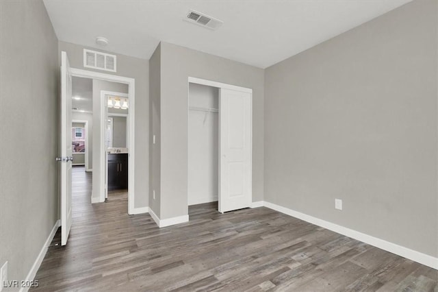 unfurnished bedroom featuring baseboards, a closet, visible vents, and wood finished floors