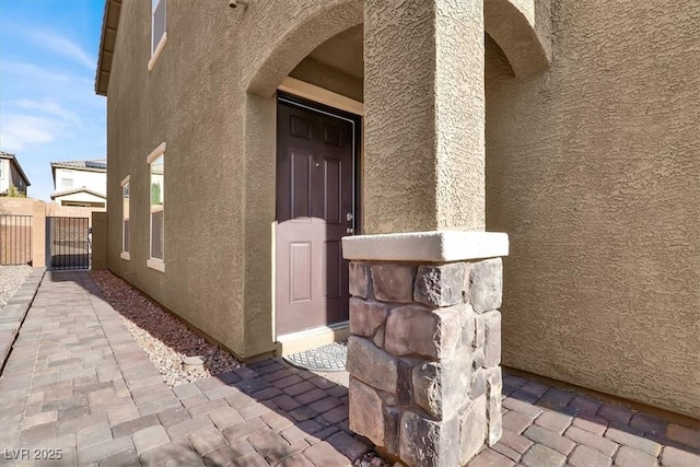 property entrance with a gate, fence, and stucco siding