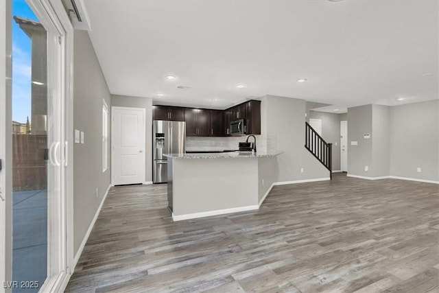 kitchen featuring dark brown cabinetry, stainless steel appliances, wood finished floors, baseboards, and decorative backsplash