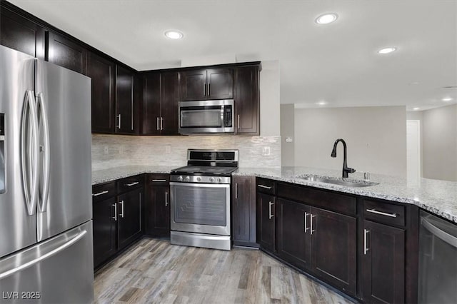 kitchen featuring light stone counters, stainless steel appliances, a sink, light wood-type flooring, and tasteful backsplash