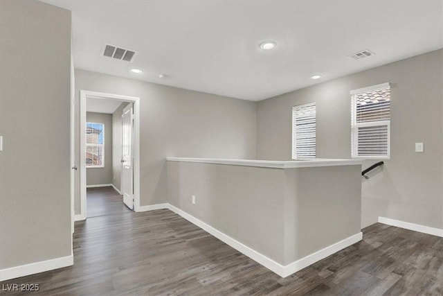 hallway with dark wood-style floors, baseboards, visible vents, and an upstairs landing