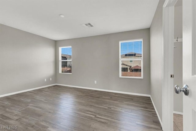 unfurnished room featuring baseboards, visible vents, and wood finished floors