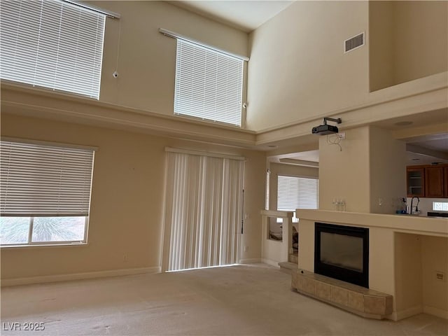 unfurnished living room featuring a tile fireplace, a towering ceiling, light colored carpet, and sink