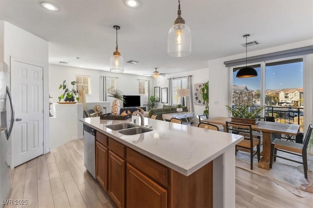 kitchen with a kitchen island with sink, dishwasher, pendant lighting, light hardwood / wood-style flooring, and sink