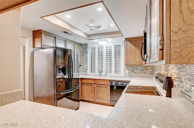 kitchen featuring black appliances, backsplash, sink, and a tray ceiling