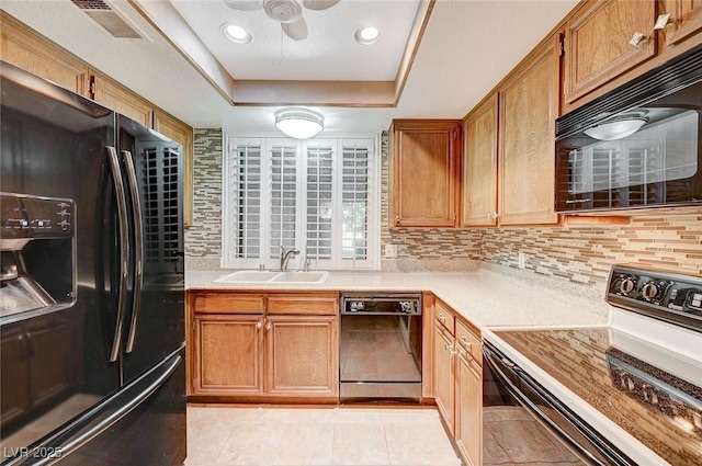 kitchen featuring sink, tasteful backsplash, a tray ceiling, light tile patterned floors, and black appliances