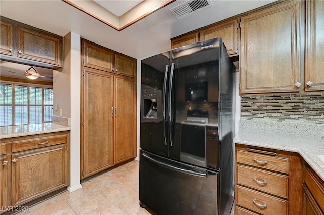 kitchen featuring decorative backsplash, black fridge with ice dispenser, light tile patterned floors, and light stone counters