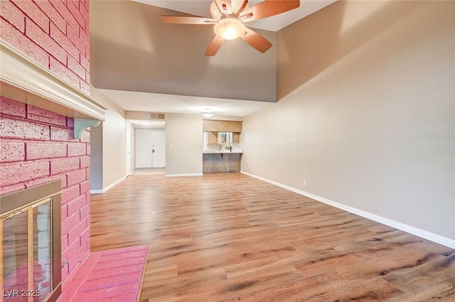 unfurnished living room with ceiling fan, a towering ceiling, wood-type flooring, and a brick fireplace