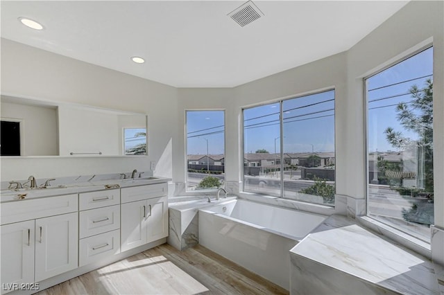 bathroom featuring hardwood / wood-style floors, vanity, and tiled bath