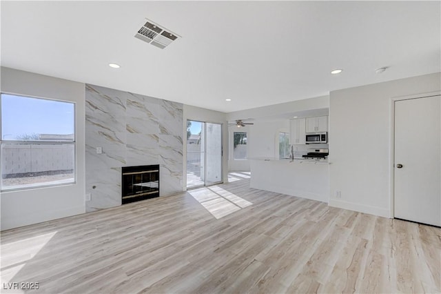 unfurnished living room featuring a premium fireplace, light hardwood / wood-style flooring, and ceiling fan