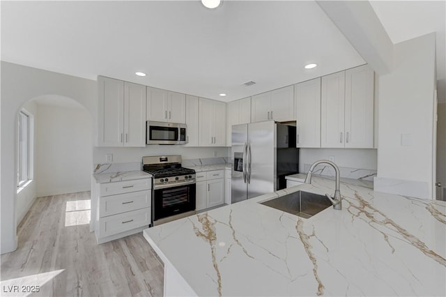 kitchen with white cabinets, sink, light hardwood / wood-style flooring, appliances with stainless steel finishes, and light stone counters